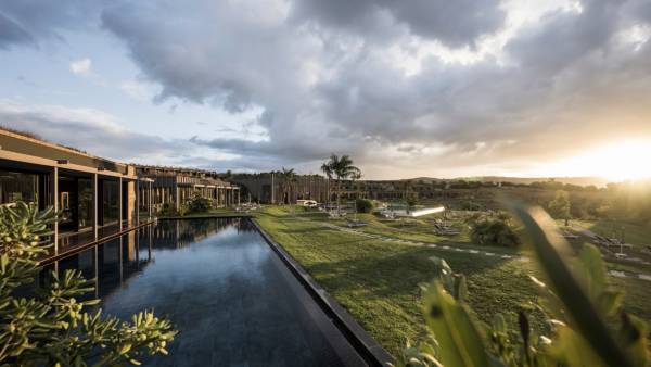 Moderner Bungalow-Komplex mit großem Pool und gepflegtem Garten unter bewölktem Himmel bei Sonnenuntergang