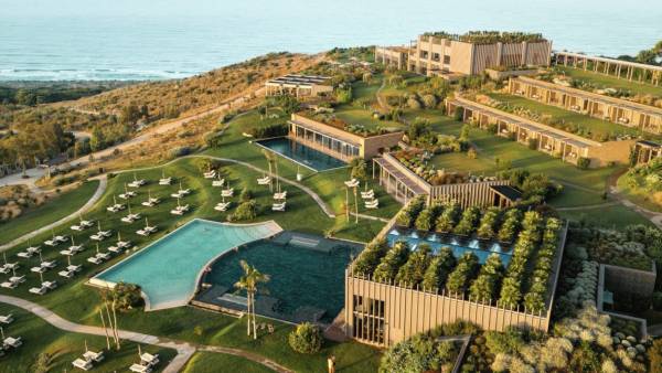 Luftaufnahme eines modernen Resorts mit mehreren Bungalows, zwei großen Schwimmbecken und Liegestühlen, gelegen an einer Küste mit Blick auf das Meer