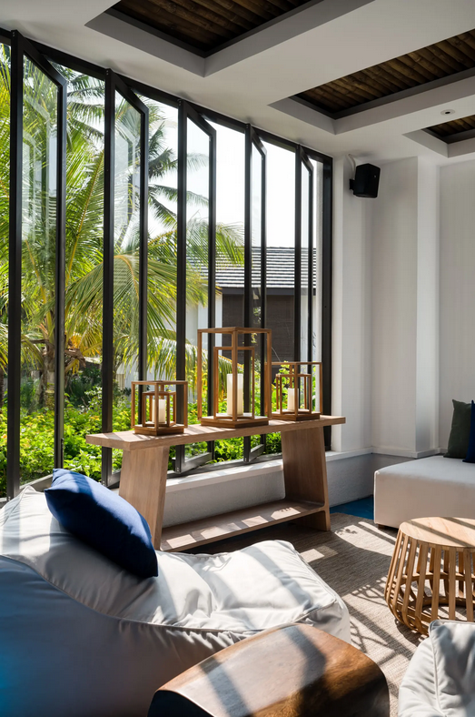 Lichtdurchfluteter Lounge-Bereich mit großen Fenstern, weißen Sitzsäcken, Holzmöbeln und Blick auf tropische Pflanzen im Boutique-Hotel in Sri Lanka