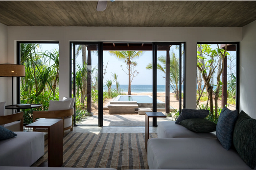 Blick aus einem modernen Hotelzimmer mit Sofa und Sesseln auf einen Pool und Palmen am Strand in Sri Lanka