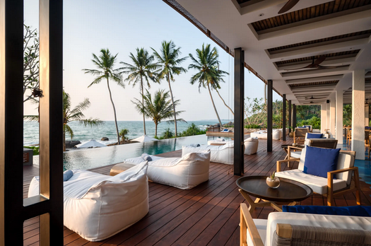 Terrasse eines Luxus-Boutique-Hotels am Strand in Sri Lanka mit Liegestühlen, Sitzmöbeln und Blick auf Palmen und das Meer