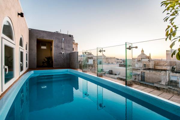 Schwimmingpool auf Dachterrasse mit Glasgeländer und Blick auf Stadtgebäude bei Sonnenuntergang