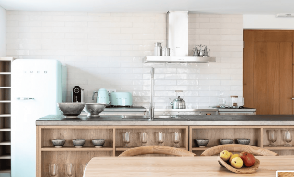 Moderne Küche in der Craverial Farmhouse Hotelanlage mit einem mintgrünen SMEG Kühlschrank, Holzregalen und einem Esstisch mit Obst.