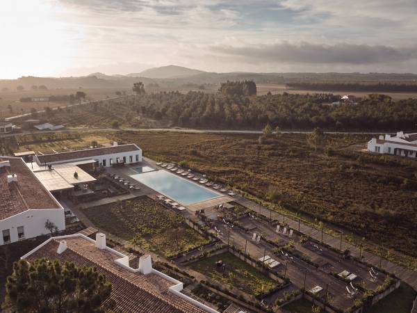 Luftaufnahme eines Hotels mit rechteckigem Pool und Gartenanlagen, umgeben von ländlicher Landschaft und Hügeln im Hintergrund