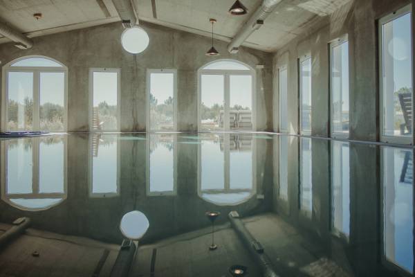 Innenansicht eines Hotelpools mit großen Fenstern, die Tageslicht hereinlassen. Der Pool spiegelt die Fenster und die Decke wieder.