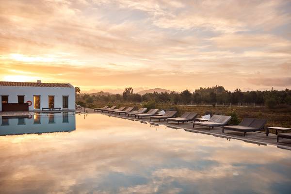Hotel mit langem Pool und Liegestühlen, Sonnenuntergang am Himmel, ruhige Landschaft im Hintergrund