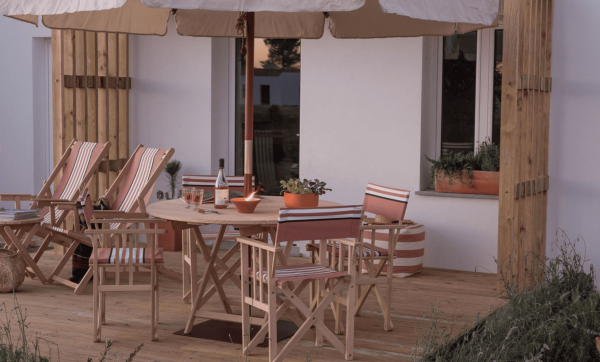 Terrasse eines Hotels mit Holztisch, Stühlen mit gestreiften Polstern und großem Sonnenschirm
