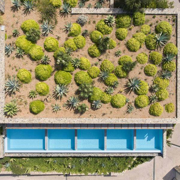 Luftaufnahme einer Hotelanlage mit einem Poolbereich. Der Pool ist rechteckig und blau, umgeben von grünen Pflanzen und Sträuchern in verschiedenen Formen.