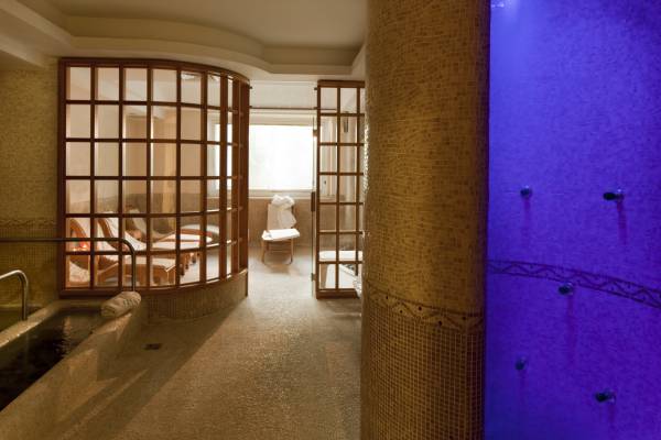 Wellnessbereich mit Mosaikfliesen, beheiztem Pool und Ruheraum mit Liegestühlen hinter Glaswänden