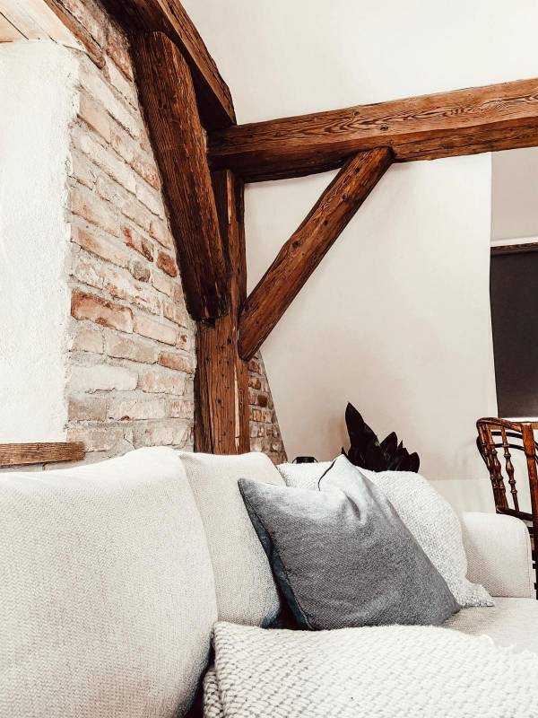 Detailaufnahme eines gemütlichen Hotelzimmers mit einem hellen Sofa, einem grauen Kissen und sichtbaren Holzstützen an der Wand.