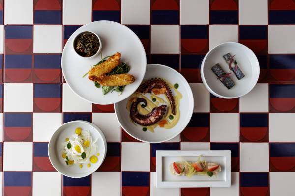 Verschiedene Gourmetgerichte auf weißen Tellern, darunter gegrillter Oktopus, frittierte Speisen und Sushi, auf einem gemusterten Tisch im Hotelrestaurant