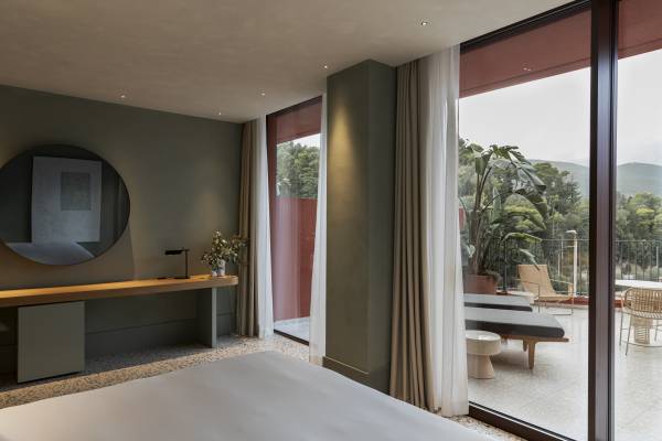 Hotelzimmer mit großem Bett, runder Wandspiegel, Schreibtisch und Terrasse mit Blick auf Bäume und Berge