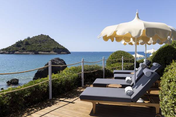 Hotelterrasse mit Liegestühlen und Sonnenschirmen mit Blick auf das Meer und eine bewaldete Insel