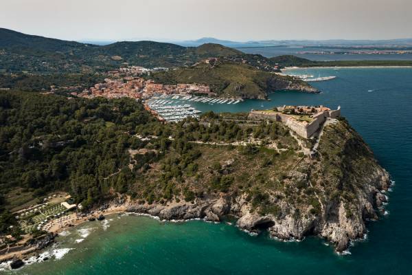 Luftaufnahme eines Hotels an der Küste mit bewaldeten Hügeln, Yachthafen und Klippen am Meer
