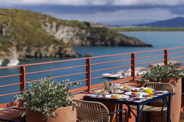 Frühstückstisch mit Orangensaft, Kaffee und Gebäck auf Hotelterrasse mit Blick auf Küste und Meer