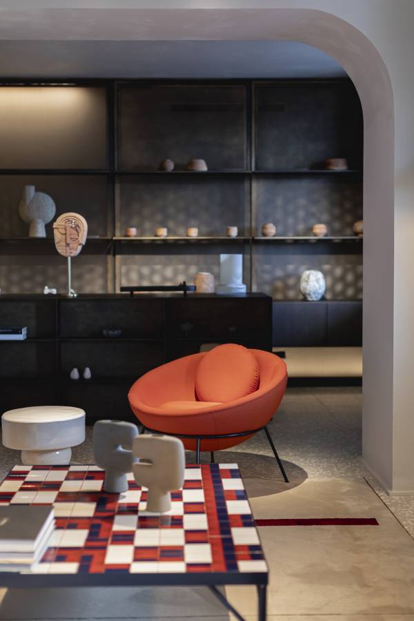 Moderne Hotellobby mit orangefarbenem Sessel, gemustertem Tisch und dekorativen Skulpturen auf Regalen