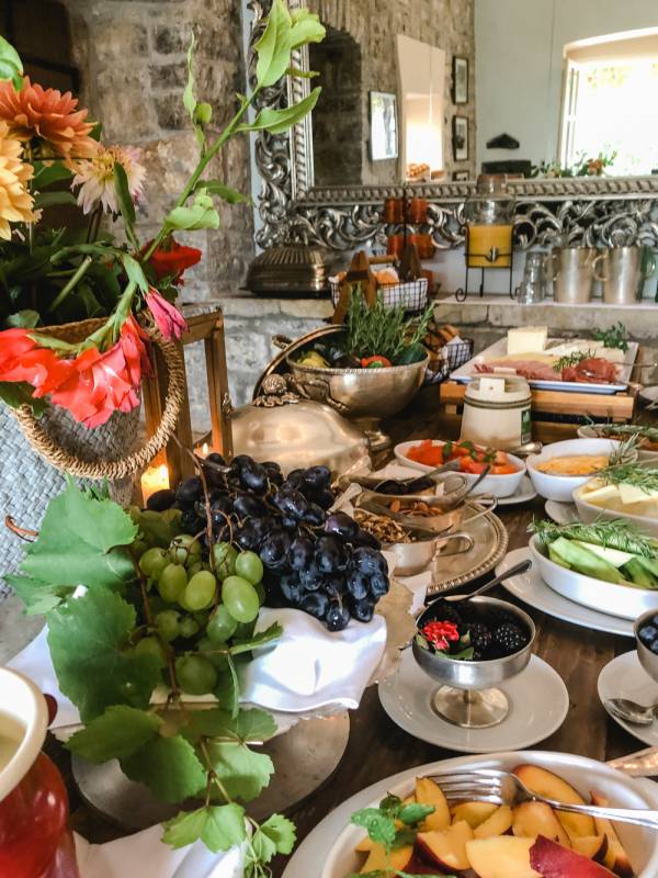 Frühstücksbuffet im Hotel mit frischen Trauben, Obst, Gemüse, Käse und dekorativen Blumen in einem rustikalen Raum