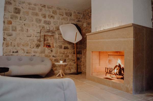 Gemütlicher Hotel-Loungebereich mit Steinwand, moderner Stehlampe, grauem Sofa und brennendem Kamin