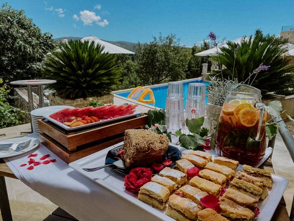 Tisch mit frischen Früchten, Kuchen und einem Krug Eistee neben Pool und Sonnenschirmen im Hotelgarten