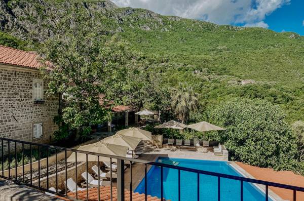 Außenpool mit Liegestühlen und Sonnenschirmen neben einem steinernen Hotelgebäude, umgeben von grünen Bergen im Hotel Malo Selo