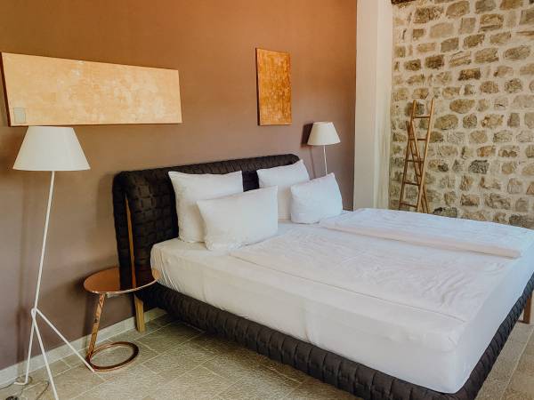Hotelzimmer mit zwei Doppelbett, weißen Bettlaken, zwei Stehlampen und Wand mit brauner Farbe und Naturstein