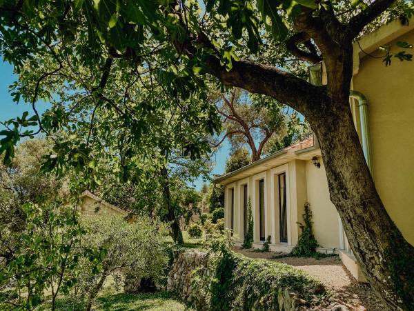 Außenansicht des Malo Selo Hotels mit gelbem Gebäude, großen Fenstern und umgeben von Bäumen und Gartenmauer