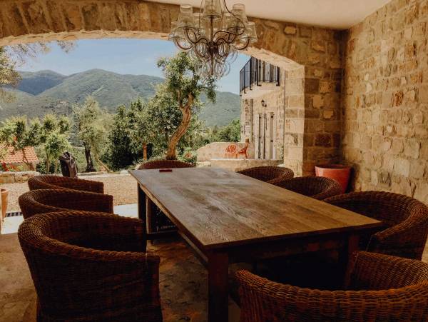 Überdachte Terrasse im Malo Selo Hotel mit großem Holztisch, acht geflochtenen Stühlen und Blick auf grüne Berge