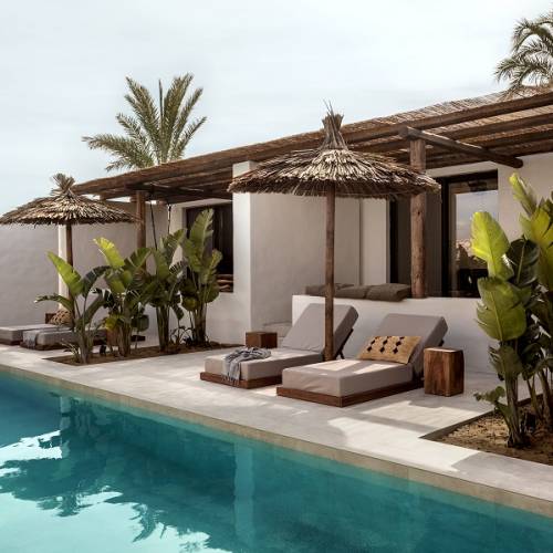 Hotelterrasse mit Pool, Liegen und Strohdächern, umgeben von tropischen Pflanzen