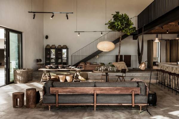 Offener Wohnbereich mit grauem Sofa, Holzmöbeln, Esstisch, Treppe und großen Fenstern in modernem Loft-Stil