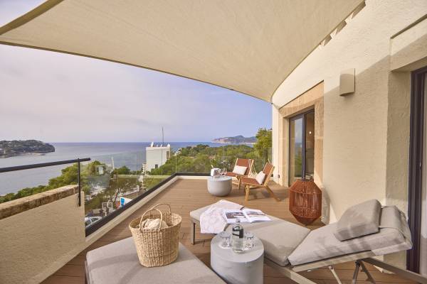 Terrasse des PUROBEACH RESORT SANTA PONSA mit Liegestühlen, Tisch, Korb und Blick auf das Meer und die Küste
