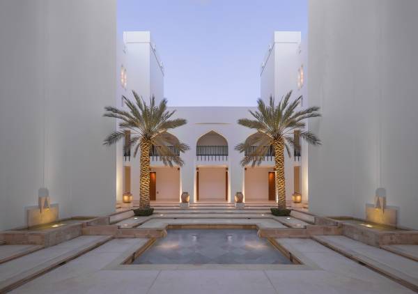 Innenhof der Hotelanlage The Chedi Muscat mit zwei Palmen, einem Wasserbecken und symmetrischen Gebäudefronten.
