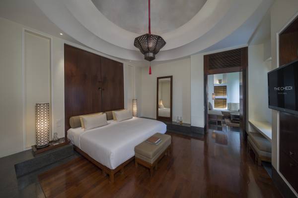 Hotelzimmer der Chedi Muscat mit einem großen Bett, zwei Nachttischen, einem Spiegel und einer modernen Lampe. Holzfußboden und helle Wände.