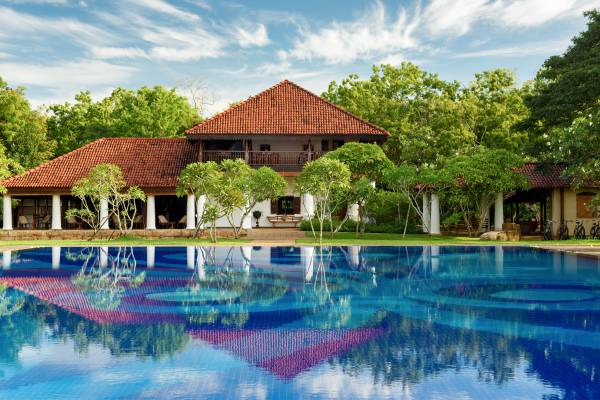 Hotel Walawwa mit rotem Ziegeldach, umgeben von Bäumen, vor einem großen blauen Pool