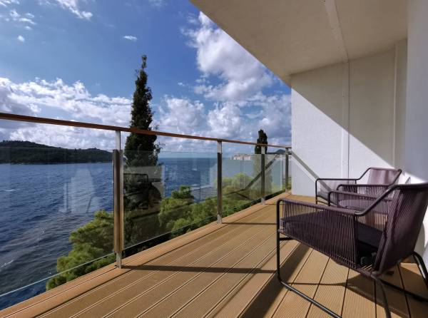 Balkon eines Superior-Zimmers mit zwei Stühlen und Glasgeländer, Blick auf Meer und bewaldete Hügel
