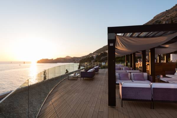 Terrasse einer Hotelbar mit Sitzgruppen und Blick auf das Meer bei Sonnenuntergang