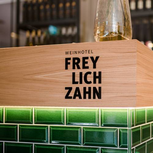Holzschild mit der Aufschrift 'WEINHOTEL FREYLICHZAHN', platziert auf einer grünen Fliesenfläche.