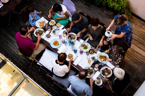 Eine Gruppe von zehn Personen sitzt an einem langen Tisch im Freien und genießt ein gemeinsames Essen. Auf dem Tisch sind verschiedene Gerichte und Getränke sichtbar.